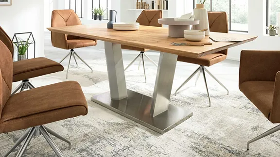 Moderner Esstisch mit Holzplatte und Metallgestell, umgeben von braunen Polsterstühlen im hellen Raum.