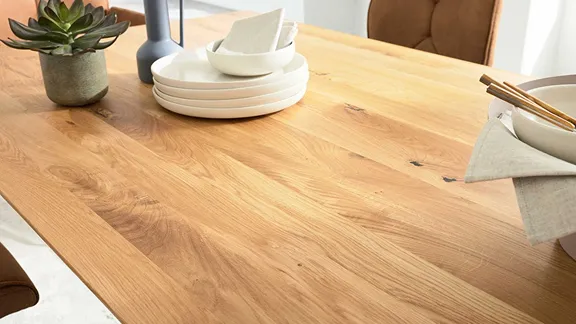 Detailaufnahme einer hellen Holz-Tischplatte mit Geschirr, Stäbchen und kleiner Pflanze.